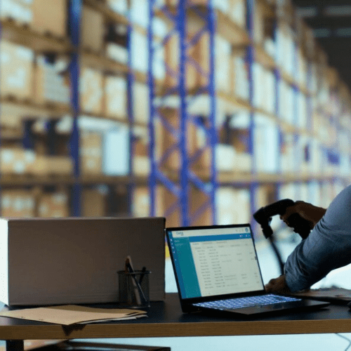 Mitarbeiter scannt Daten im Lagerbüro, im Hintergrund Hochregale mit Kartons für europaweite Logistik und Transporte.